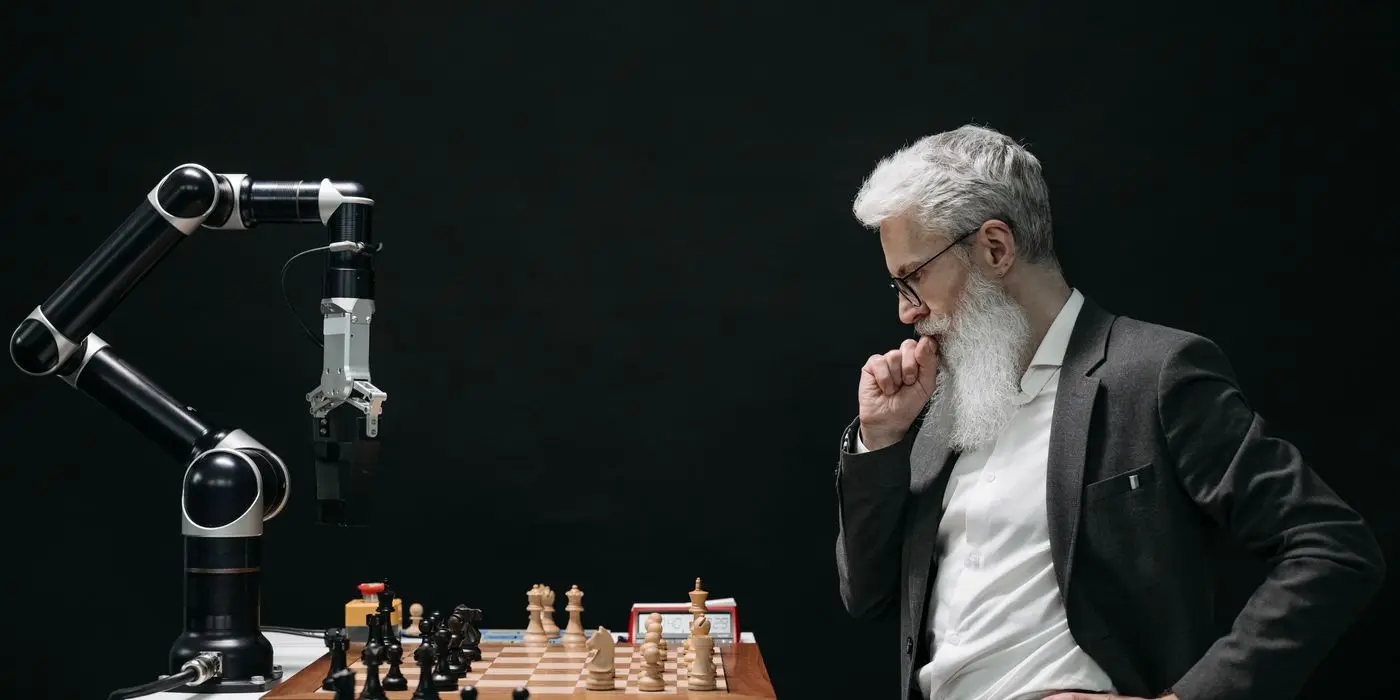A person studying a chessboard opposite a robotic arm
